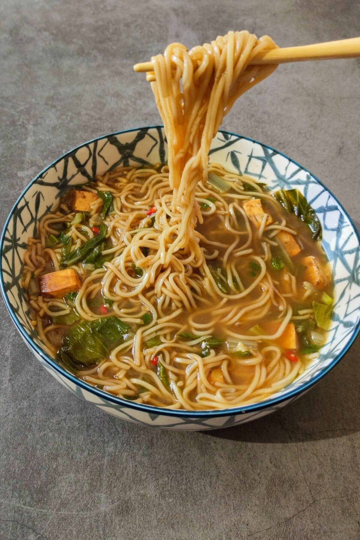 Noodles lifted with chopsticks over a bowl of Chinese noodle soup