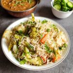 Vegetable rice in a bowl with curry and salad in the background