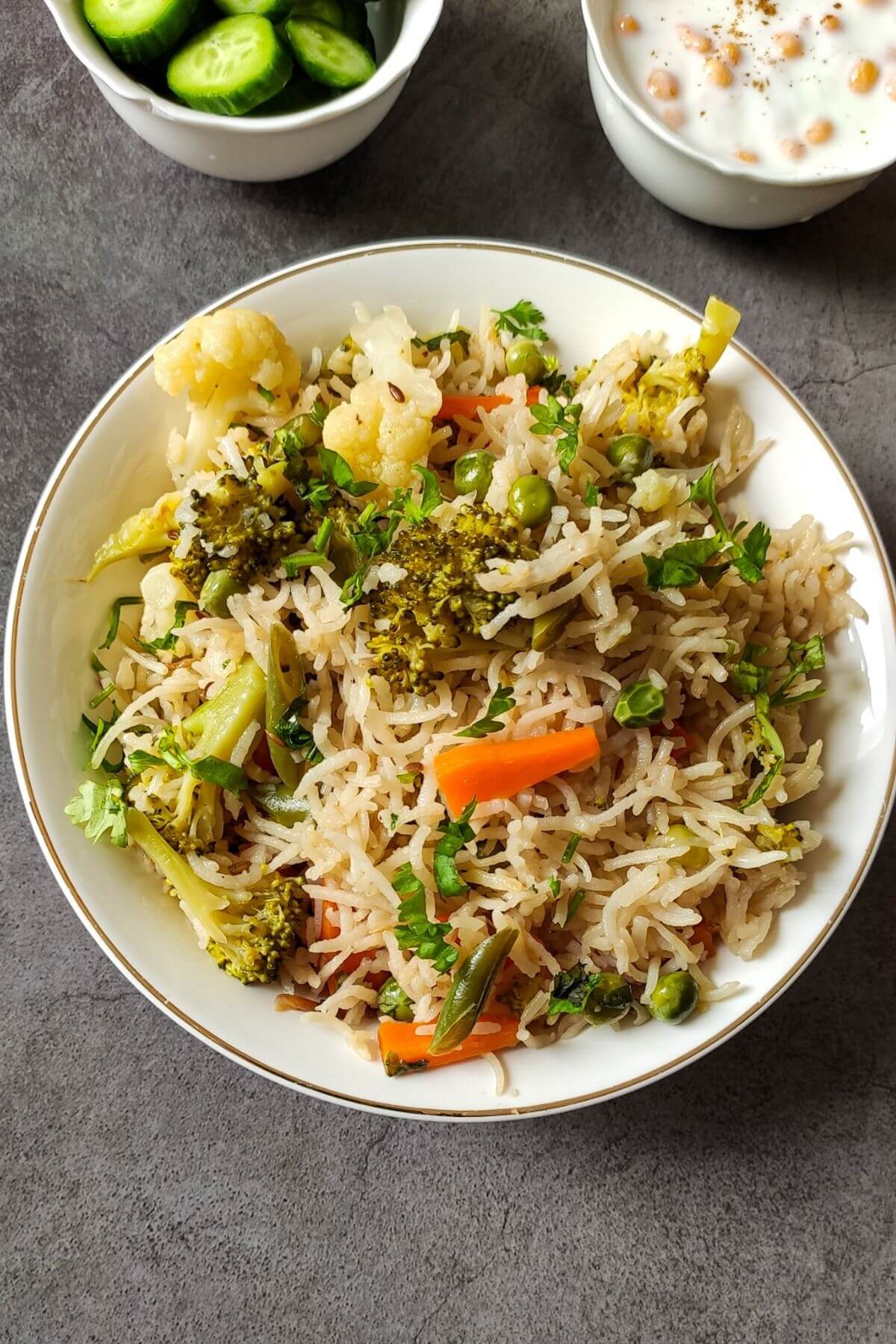 Indian vegetable rice served with raita and salad in the background