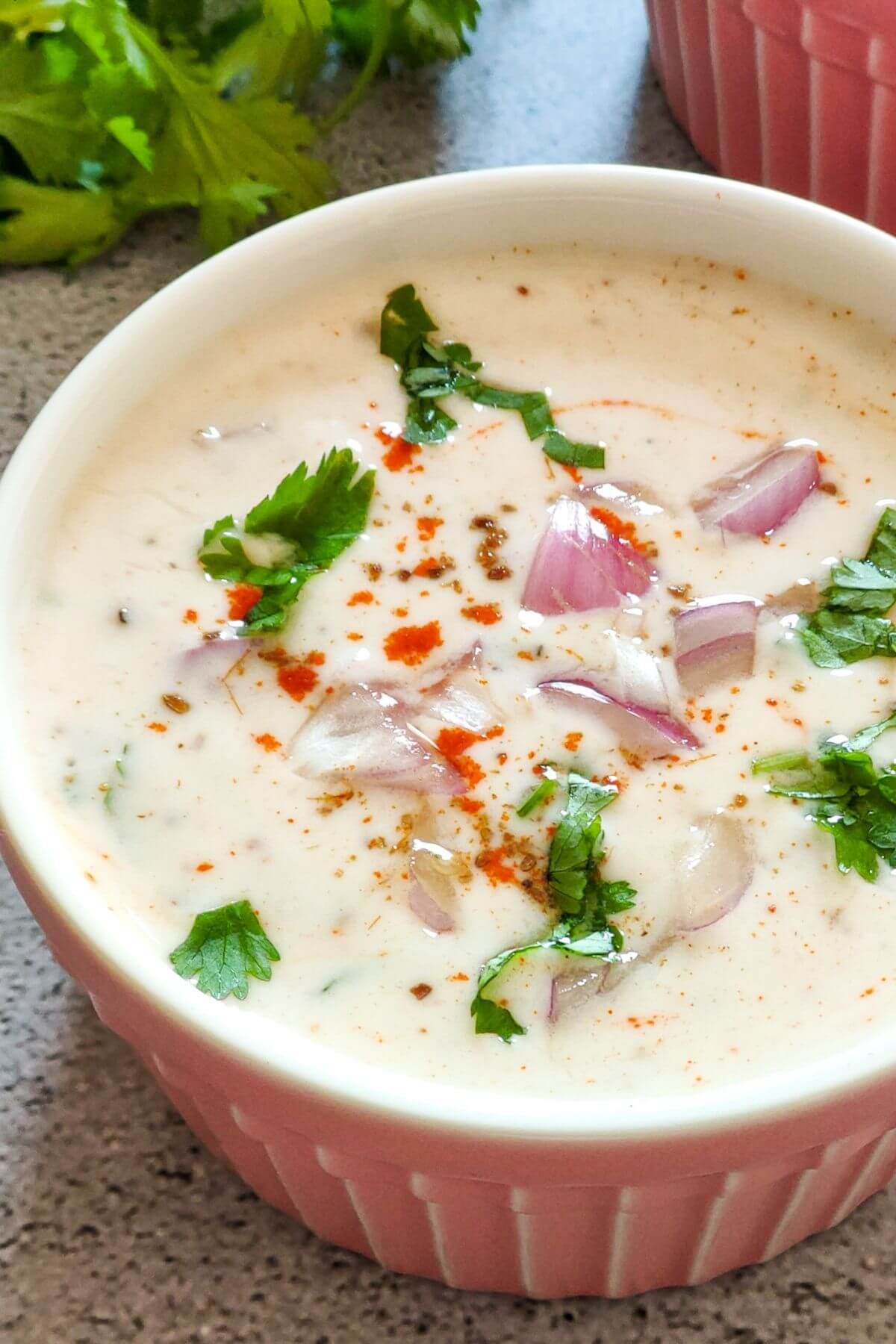 Onion raita garnished with spices and herbs in a pink bowl