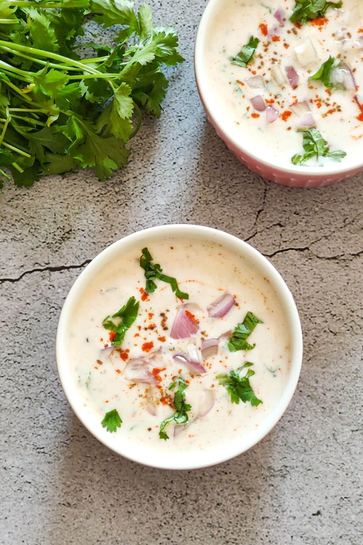 Two bowls of onion raita with fresh cilantro on the side