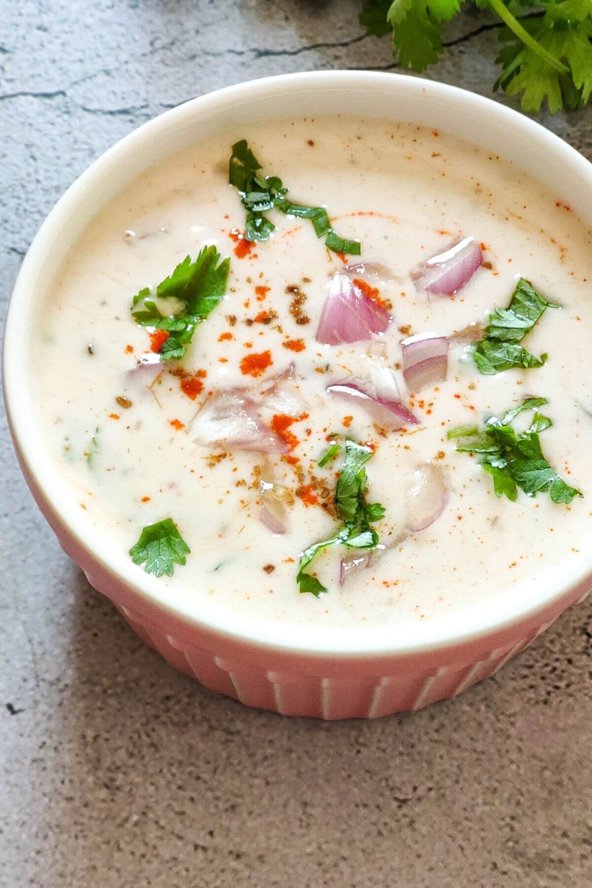 Red onion raita garnished with spices and herbs served in a bowl