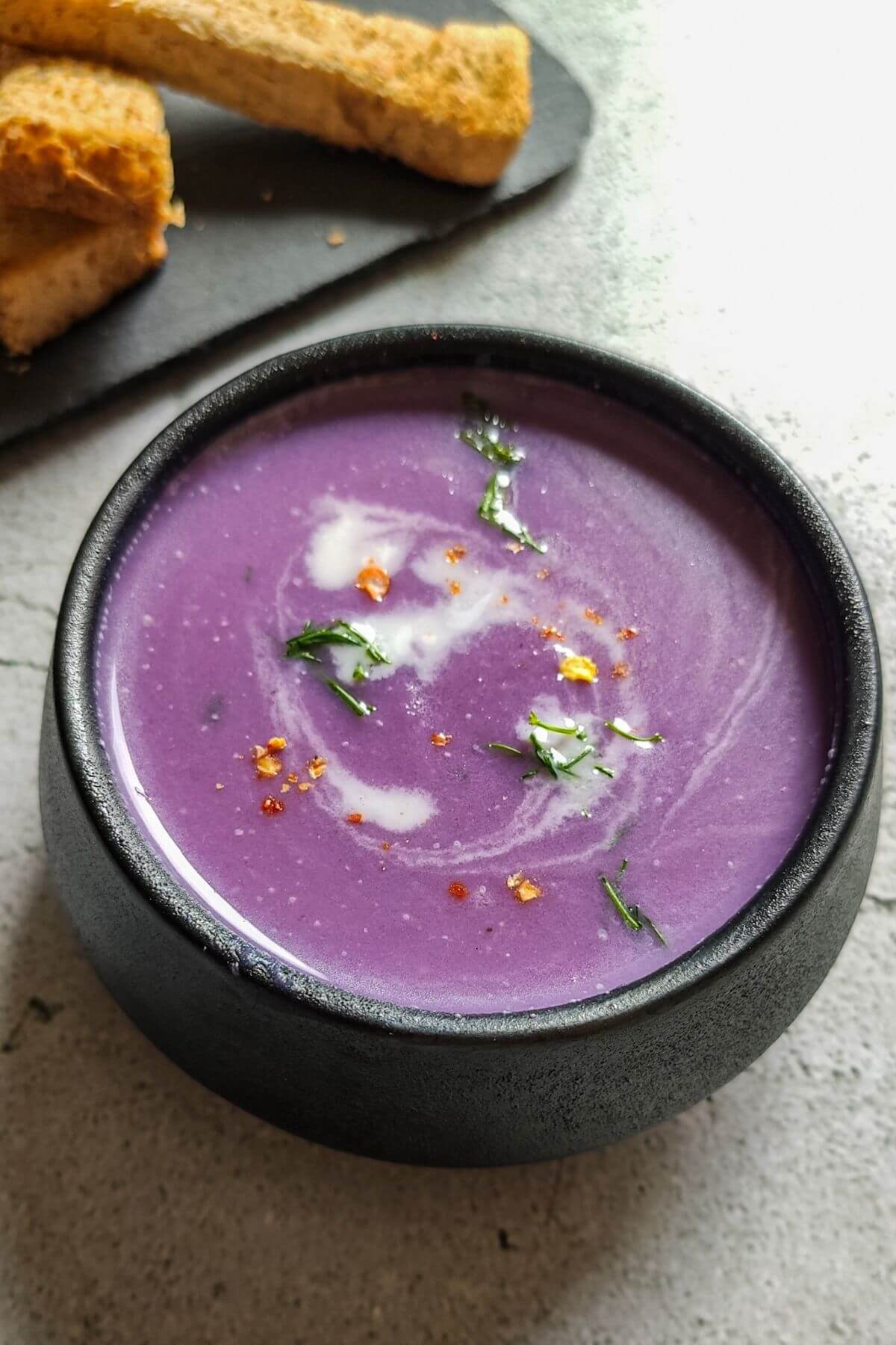 Red cabbage soup garnished with almond milk and dill served in a black bowl
