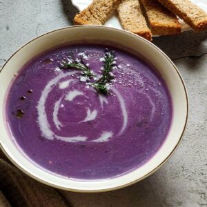 Red cabbage soup served in a white bowl with bread sticks in the background