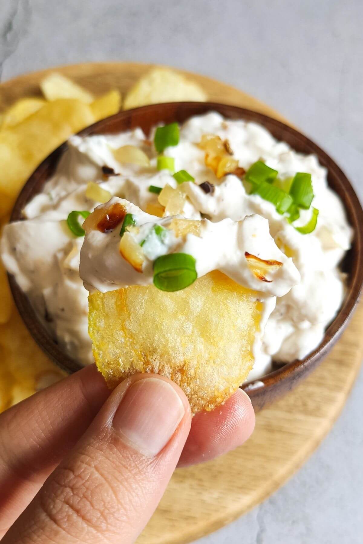 A potato chip dipped in French onion dip lifted over a bowl of dip