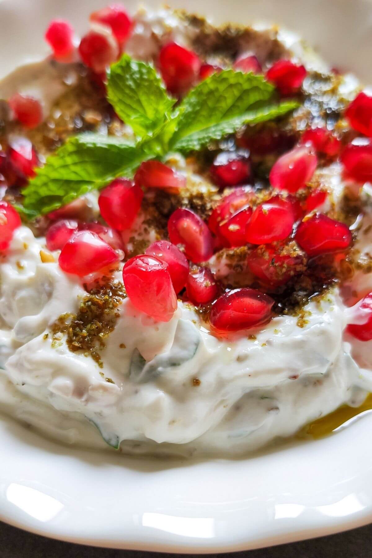 Garlic labneh dip garnished with za'atar, pomegranate arils and mint leaves