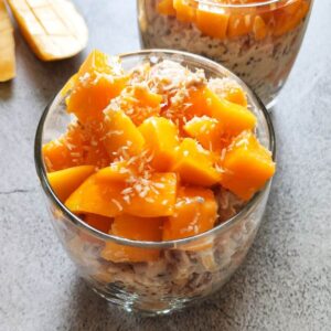 mango overnight oats served in a glass bowl another bowl and mango slices in the background