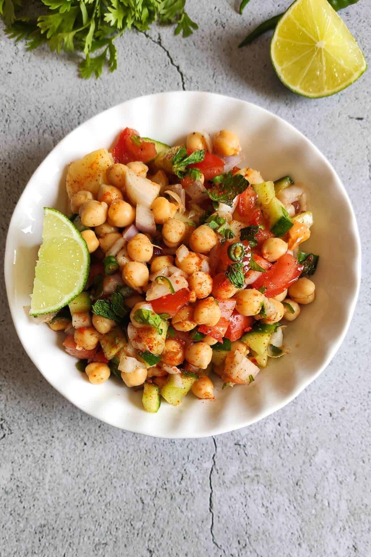 Chana salad garnished with a lime  wedge served in a white bowl