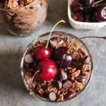 A glass bowl of vegan chocolate cherry overnight oats with another bowl of the dish and a bowl of cherries in the background