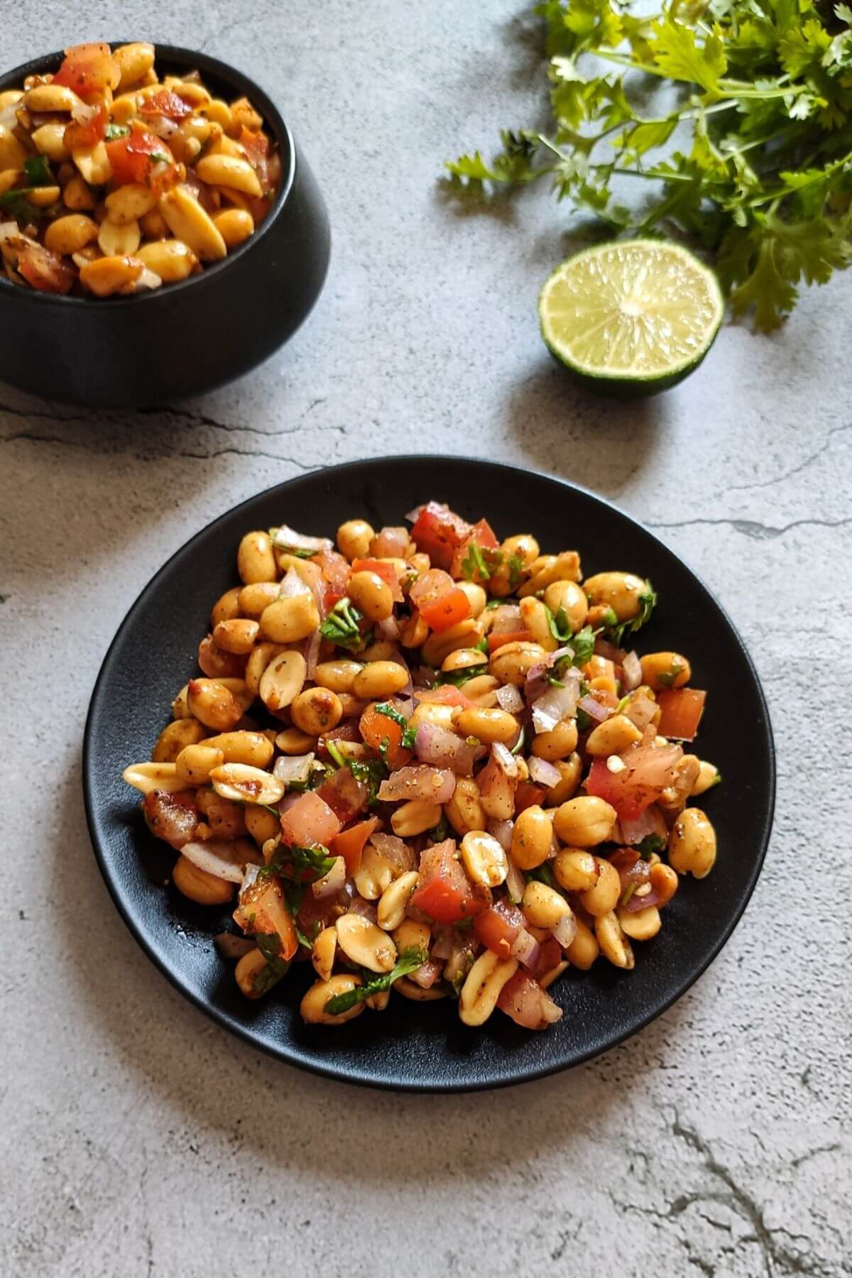 Indian masala peanuts served on a black plate with another bowl of chaat, half a lime and cilantro in the background