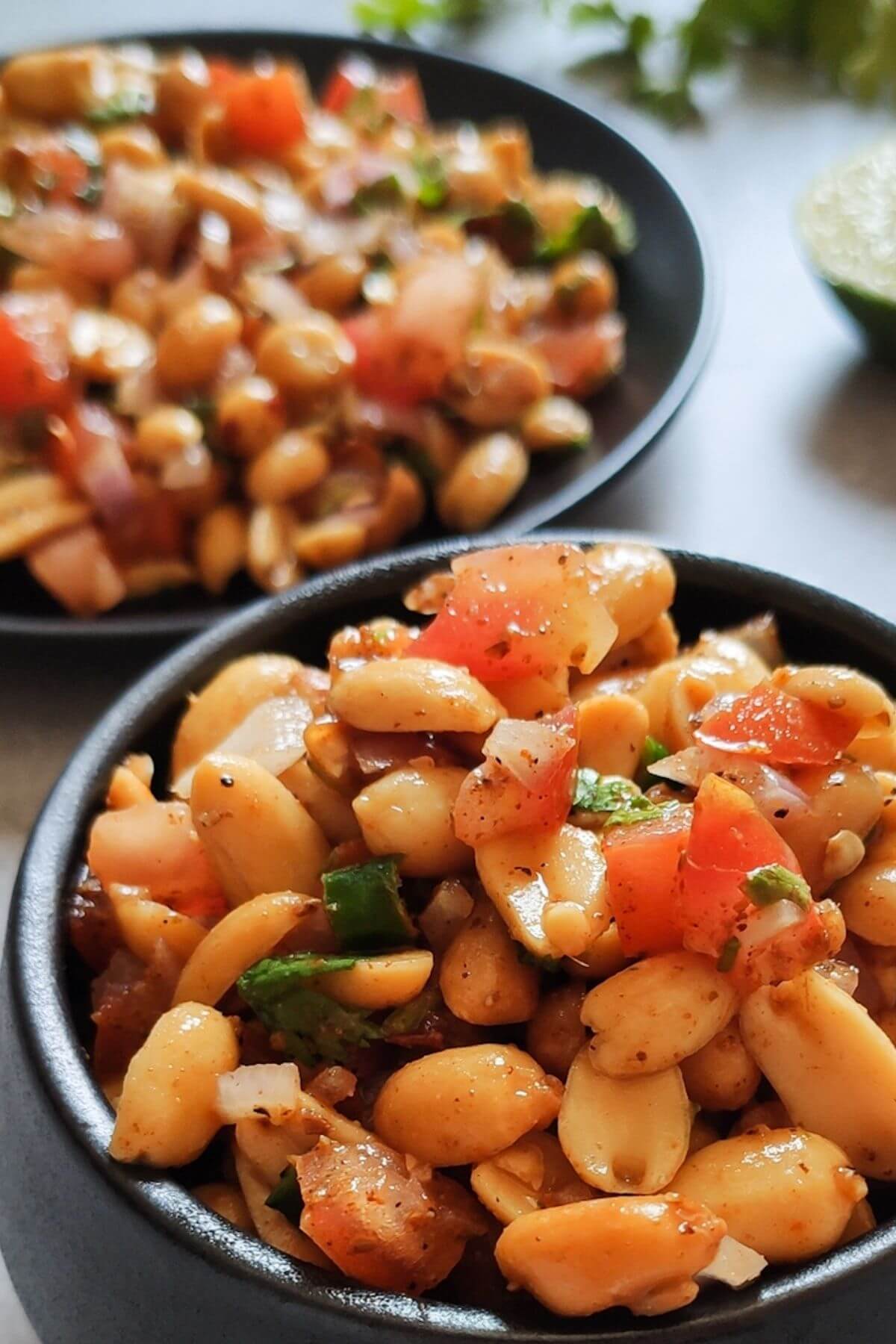 Peanut chaat served in a black bowl more chaat in the background on a plate with lime wedge and herbs