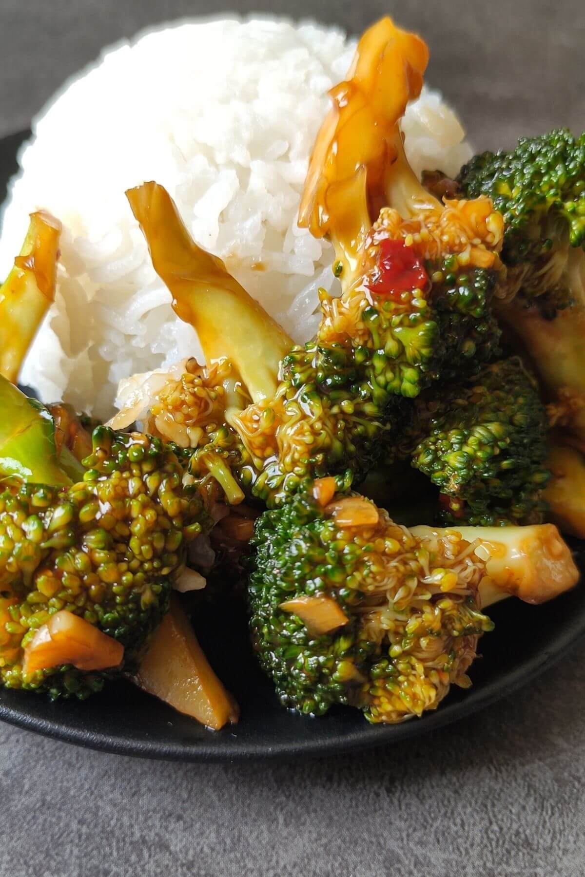 Asian style broccoli in ginger garlic sauce served with rice on a black plate