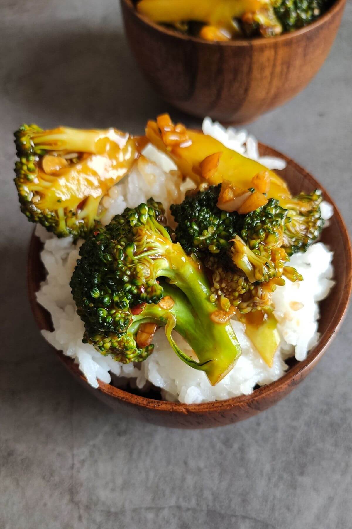 Ginger garlic broccoli served on top of cooked rice in a wooden bowl and another bowl of broccoli in the backgrounf