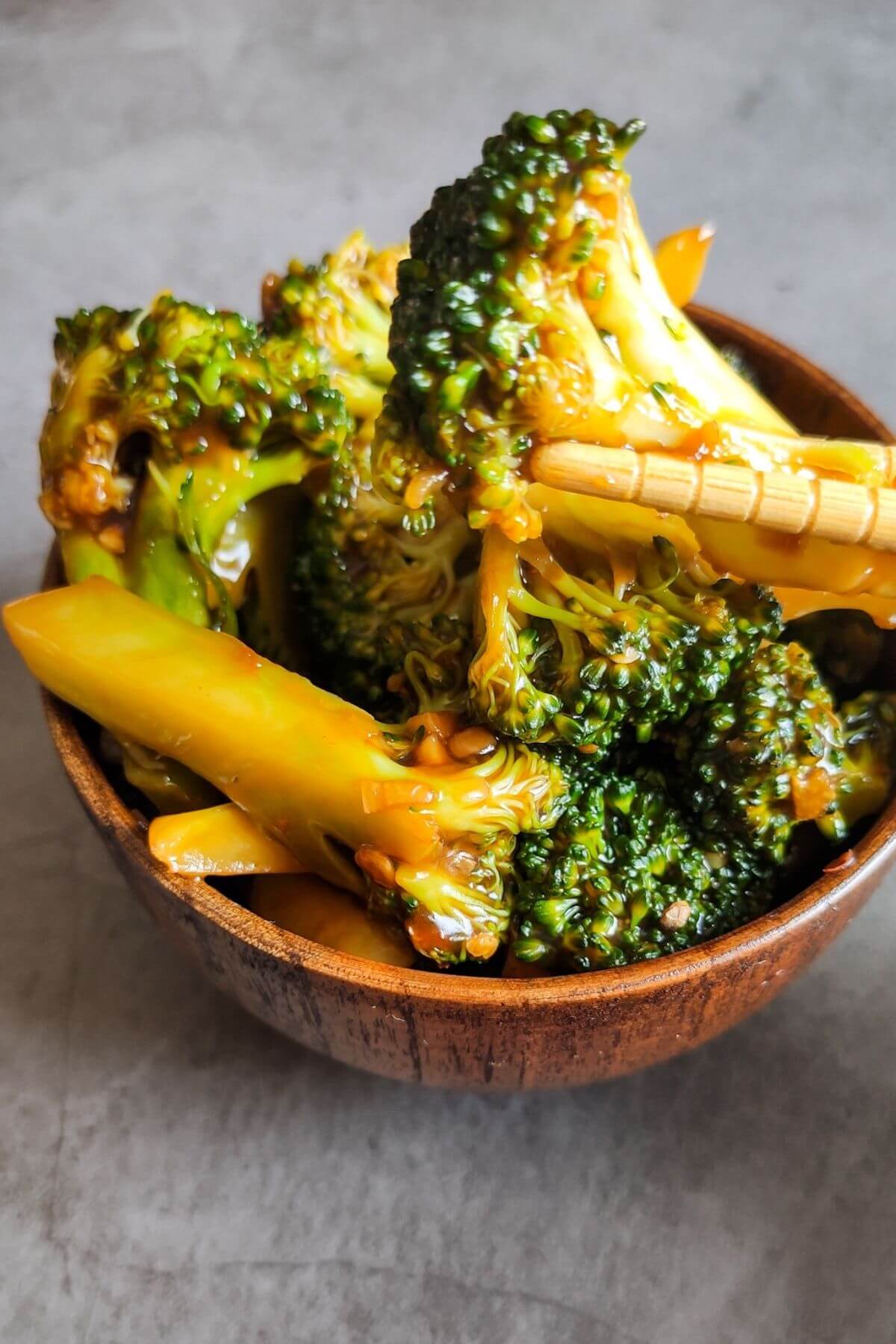 Asian garlic broccoli getting lifted with a pair of chopsticks from a wooden bowl of the dish