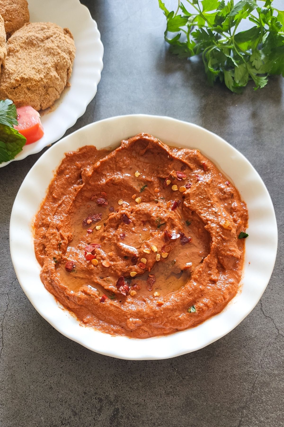 red pepper walnut dip served in a white bowl with cutlets and herbs