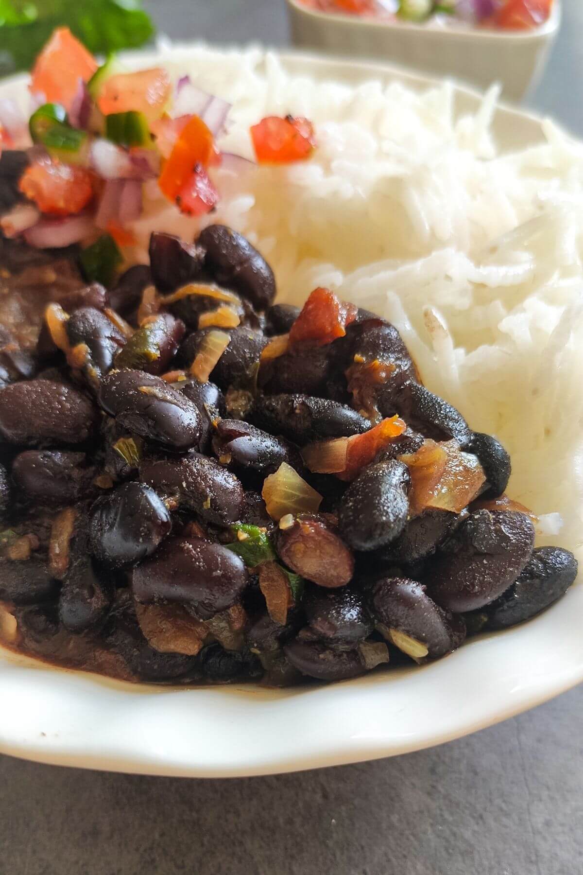 black bean curry served with rice and salad in a white bowl