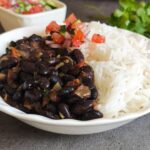 Indian black bean curry with rice and salad served in a white bowl