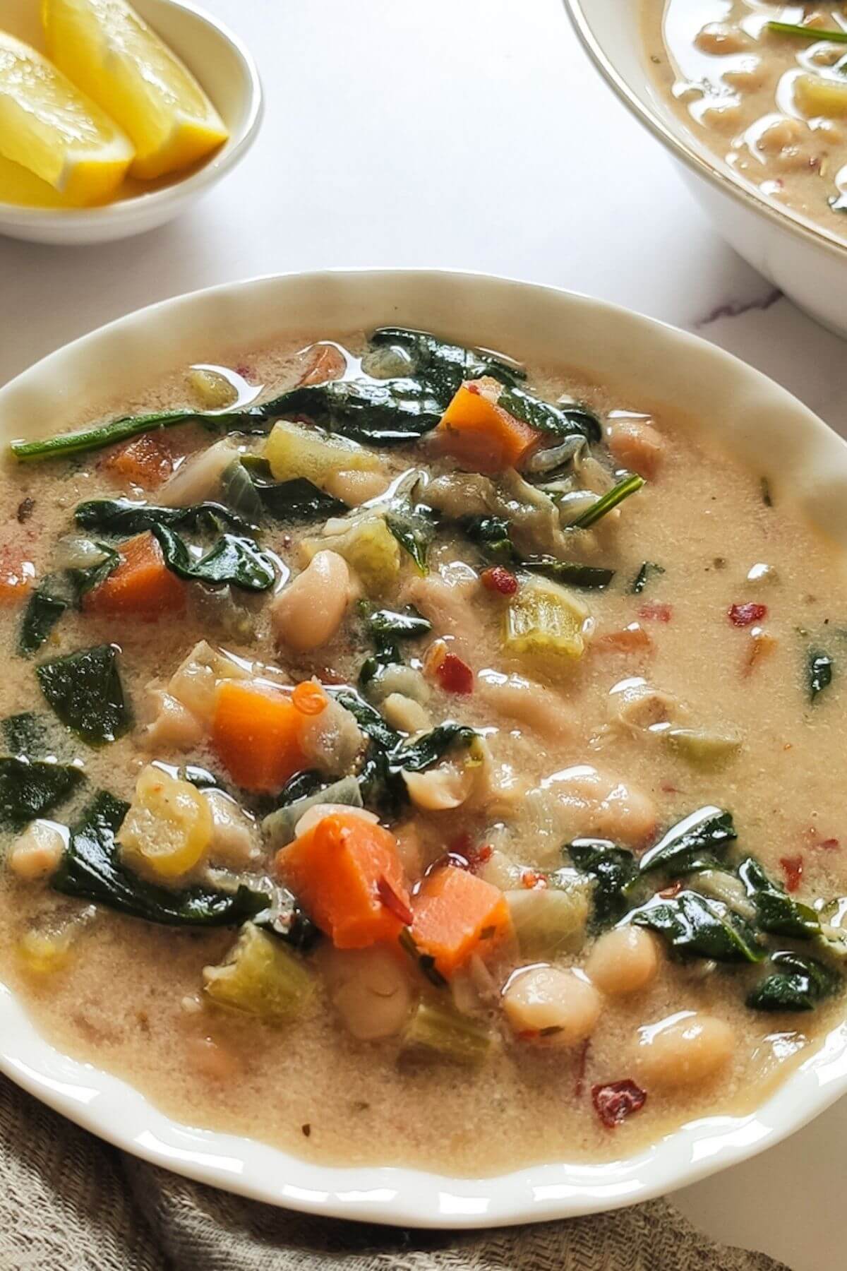 white bean vegetable soup in a bowl with lemon wedges