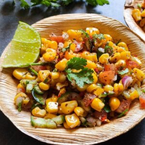 Indian corn salad garnish with a lime wedge and cilantro served in a wooden bowl.