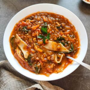 vegan lasagna soup in a white bowl with a spoon.