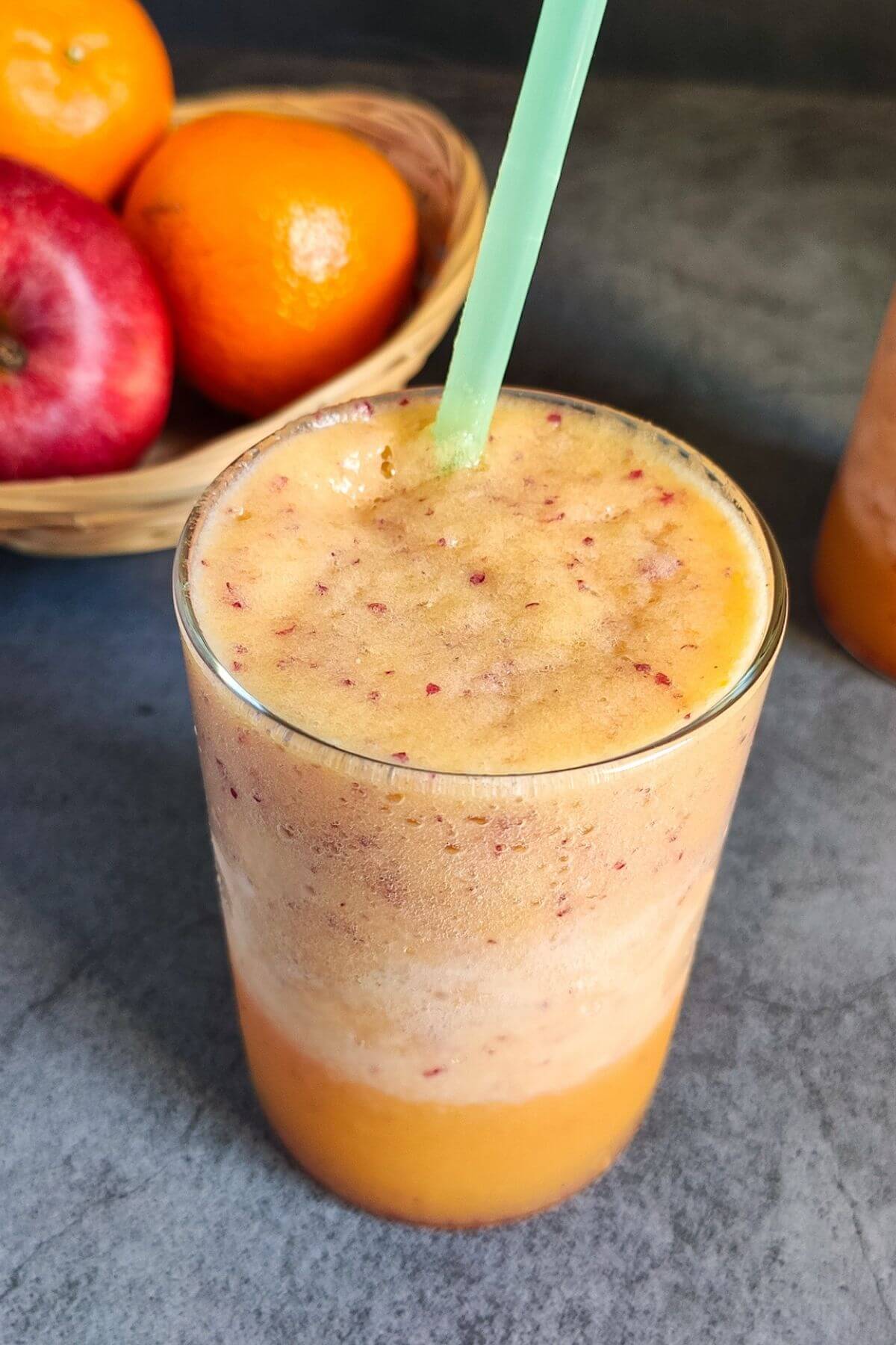 apple orange smoothie in a glass with straw and a basket of fruits.