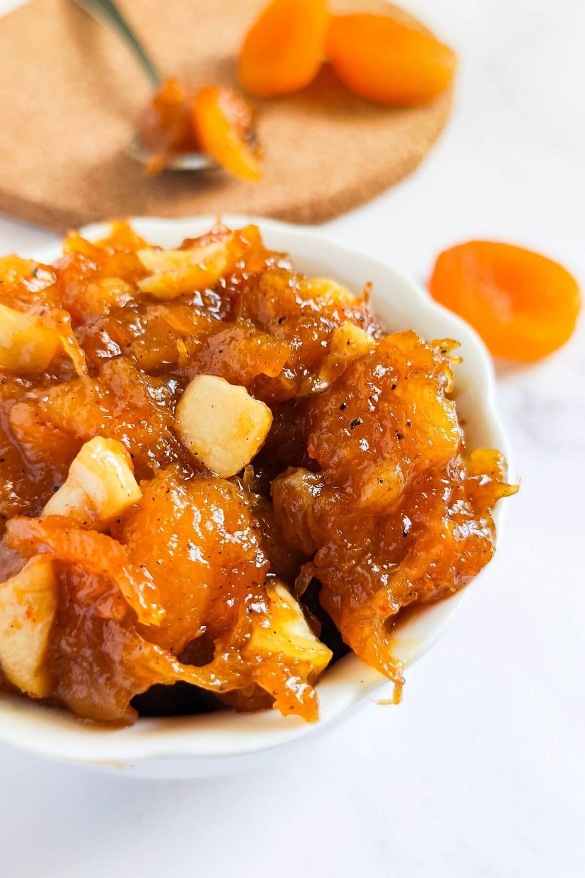 spiced apricot chutney in a white bowl with dried apricots in the background.
