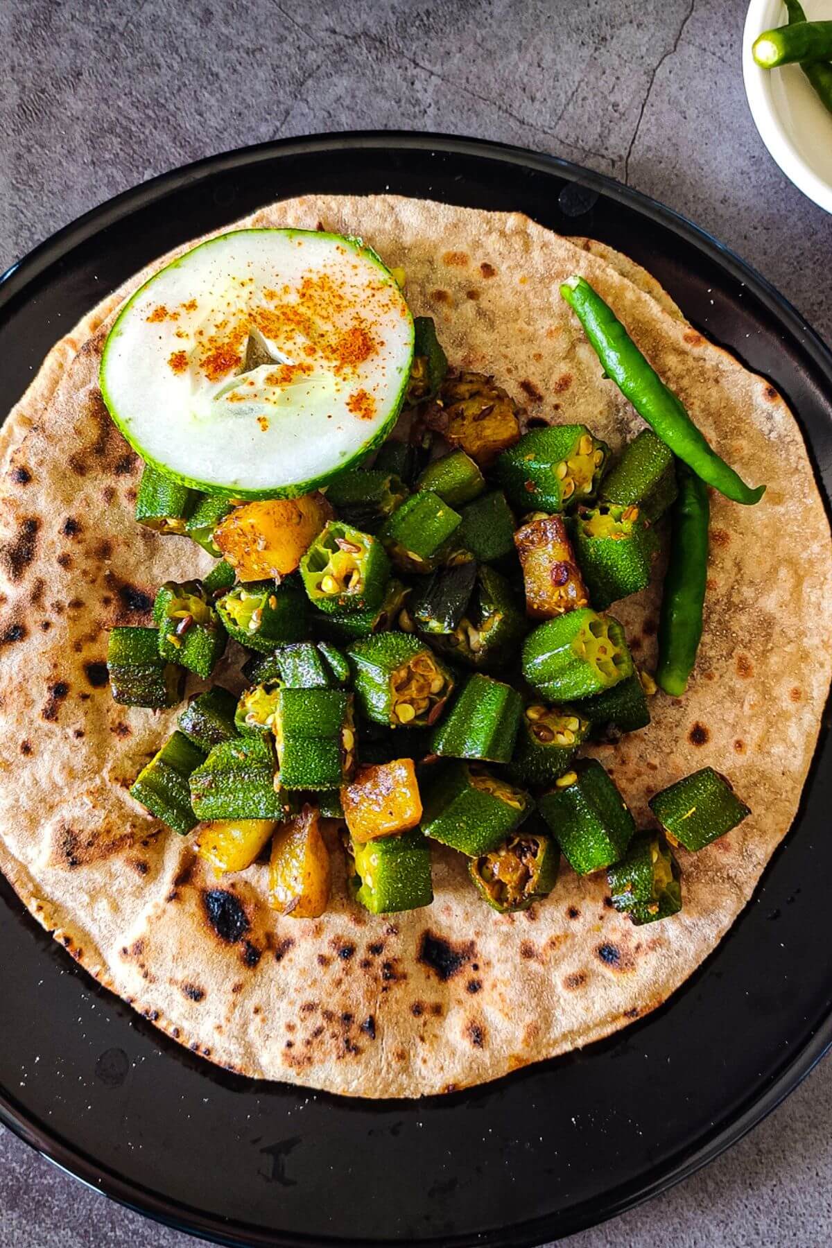 aloo bhindi sabzi served over roti with a slice of cucumber and green chilies.