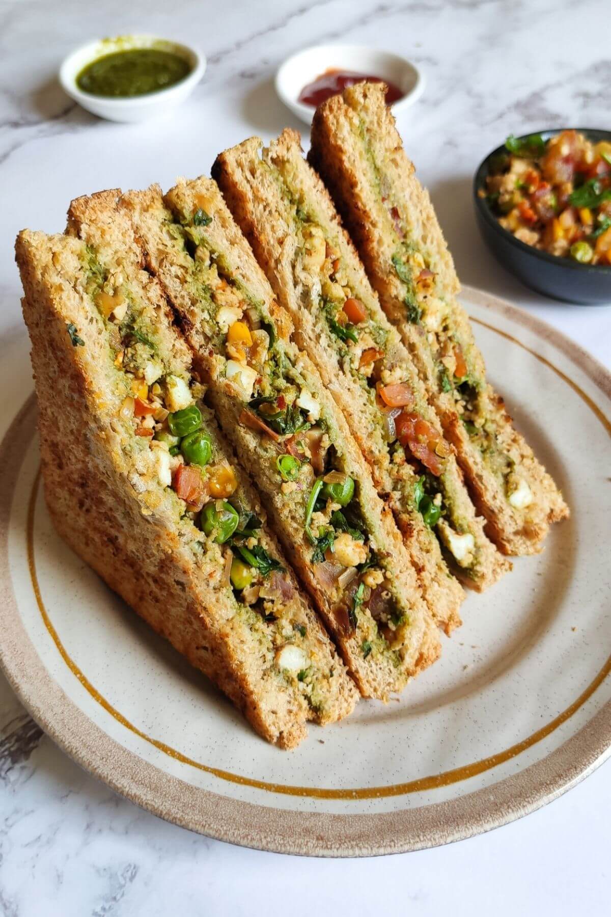 Four spicy paneer sandwiches on a plate with bowls of dipping sauce.