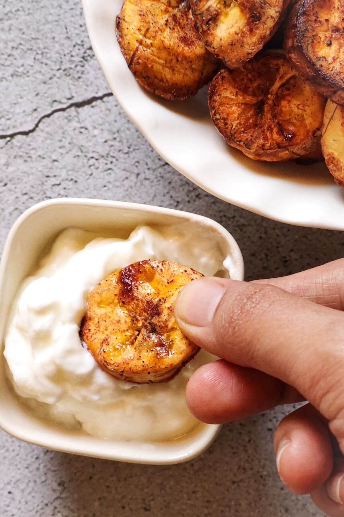 A baked plantain chip getting dipped in a bowl of yogurt.