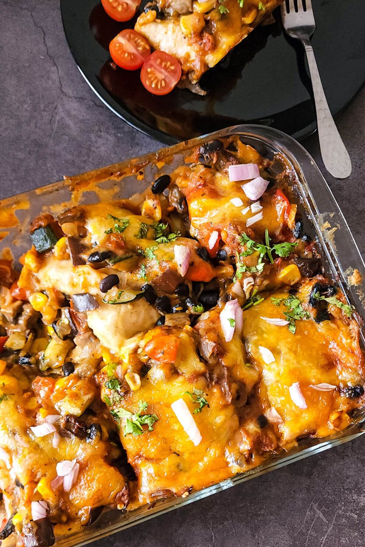 Vegetables enchilada casserole in a glass dish and more in a plate.