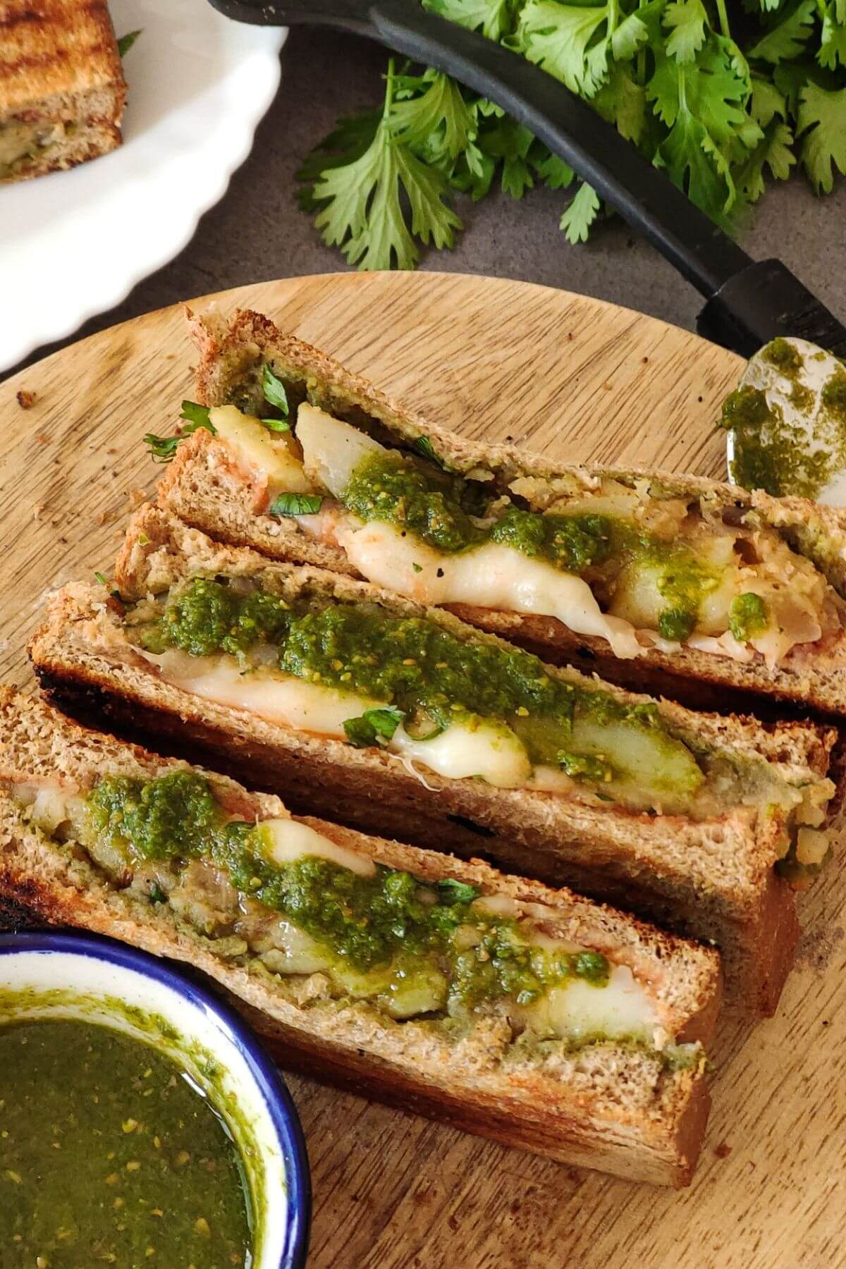 Potato sandwiches with green chutney on a wooden board.
