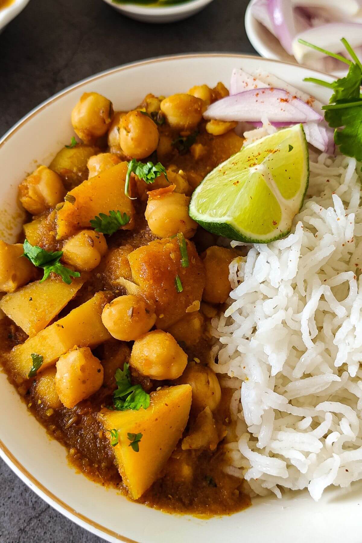 curried potatoes and chickpeas served in a bowl with rice, a slice of lime and onion slices.