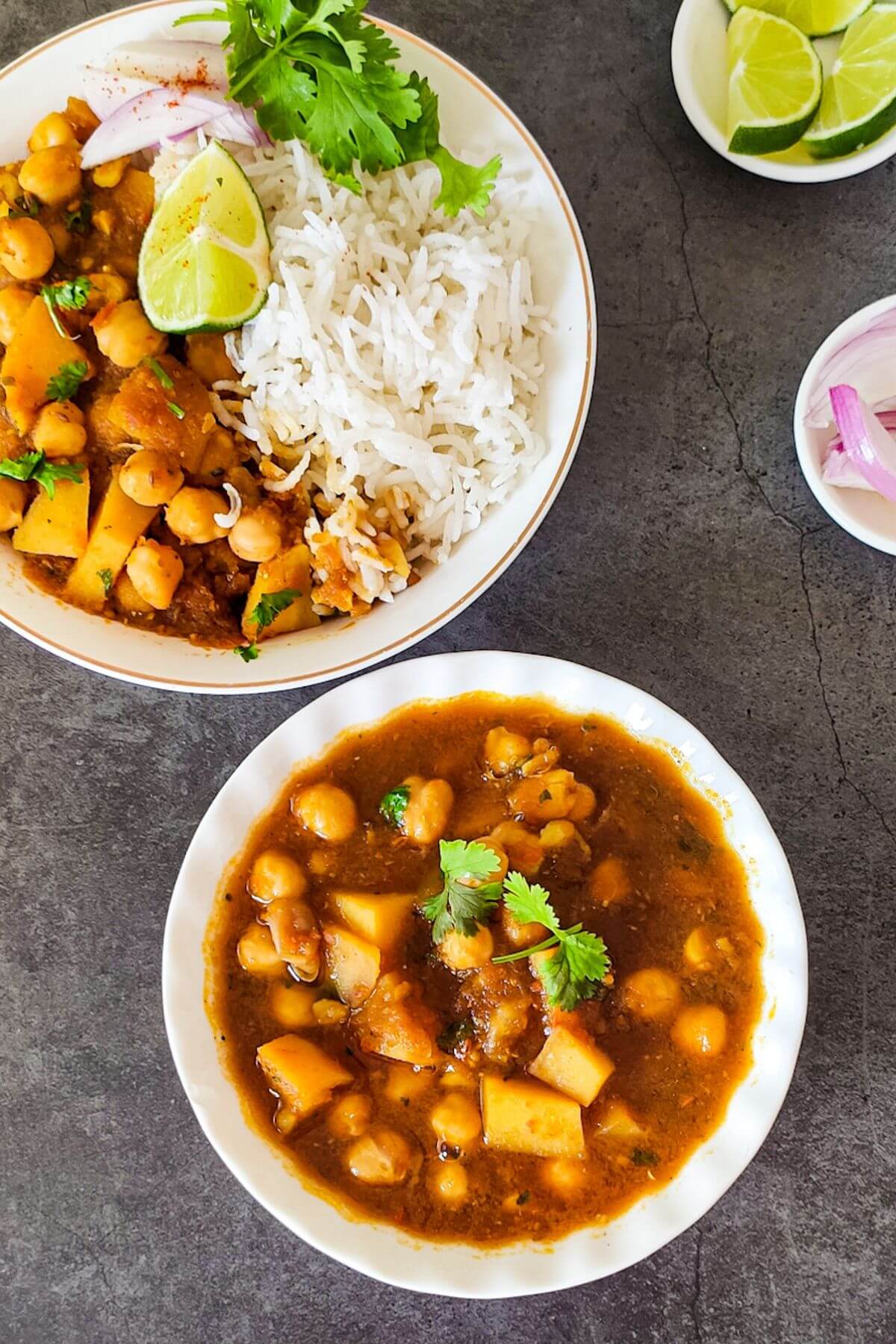 A bowl of chickpea potato curry with another bowl of rice and curry in the background.