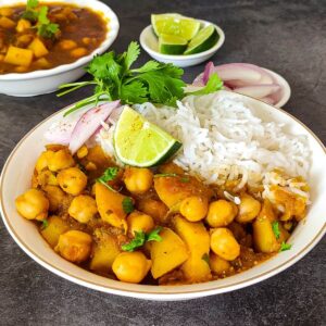 Chickpea potato curry served in a bowl with rice, onion slices, cilantro, and a slice of lime.