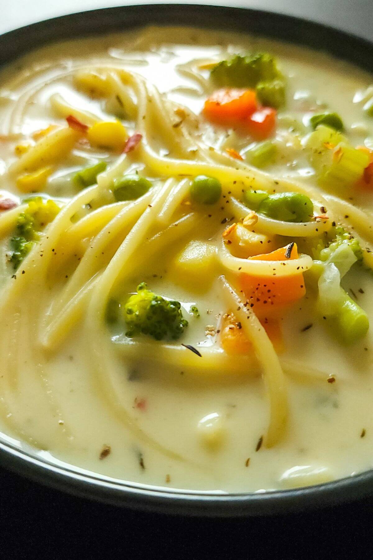 Cream of vegetable soup with noodles in a black bowl.