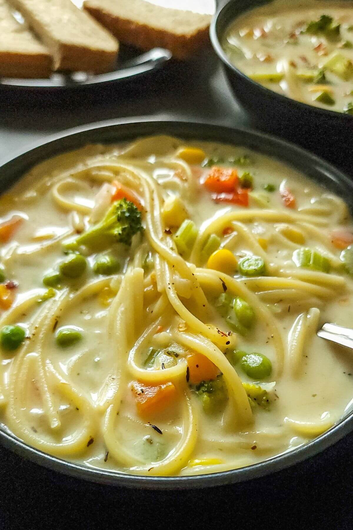 Two bowls of creamy noodle soup with bread in the background.