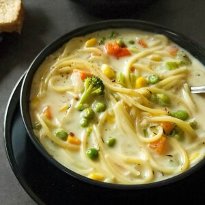Creamy vegetable noodle soup in a black bowl.