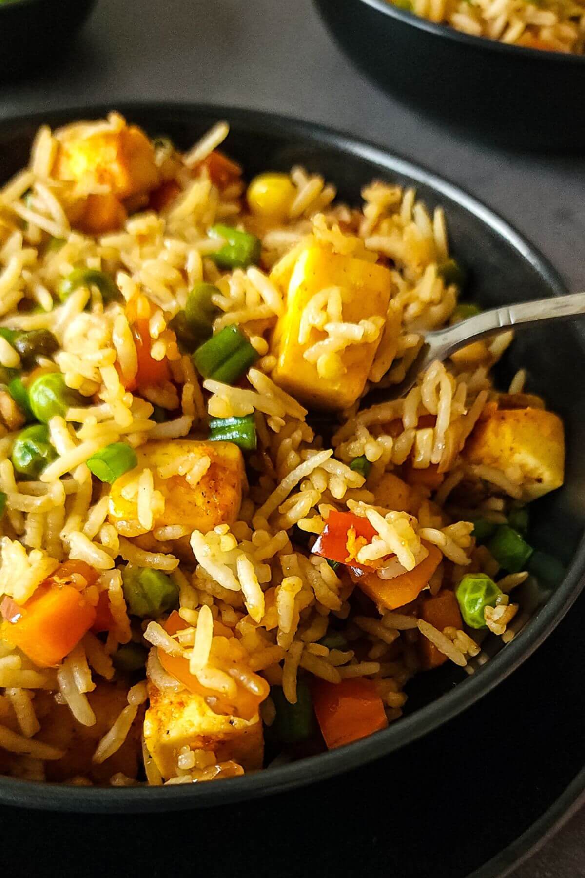 Vegetarian paneer fried rice in a black bowl with a spoon.