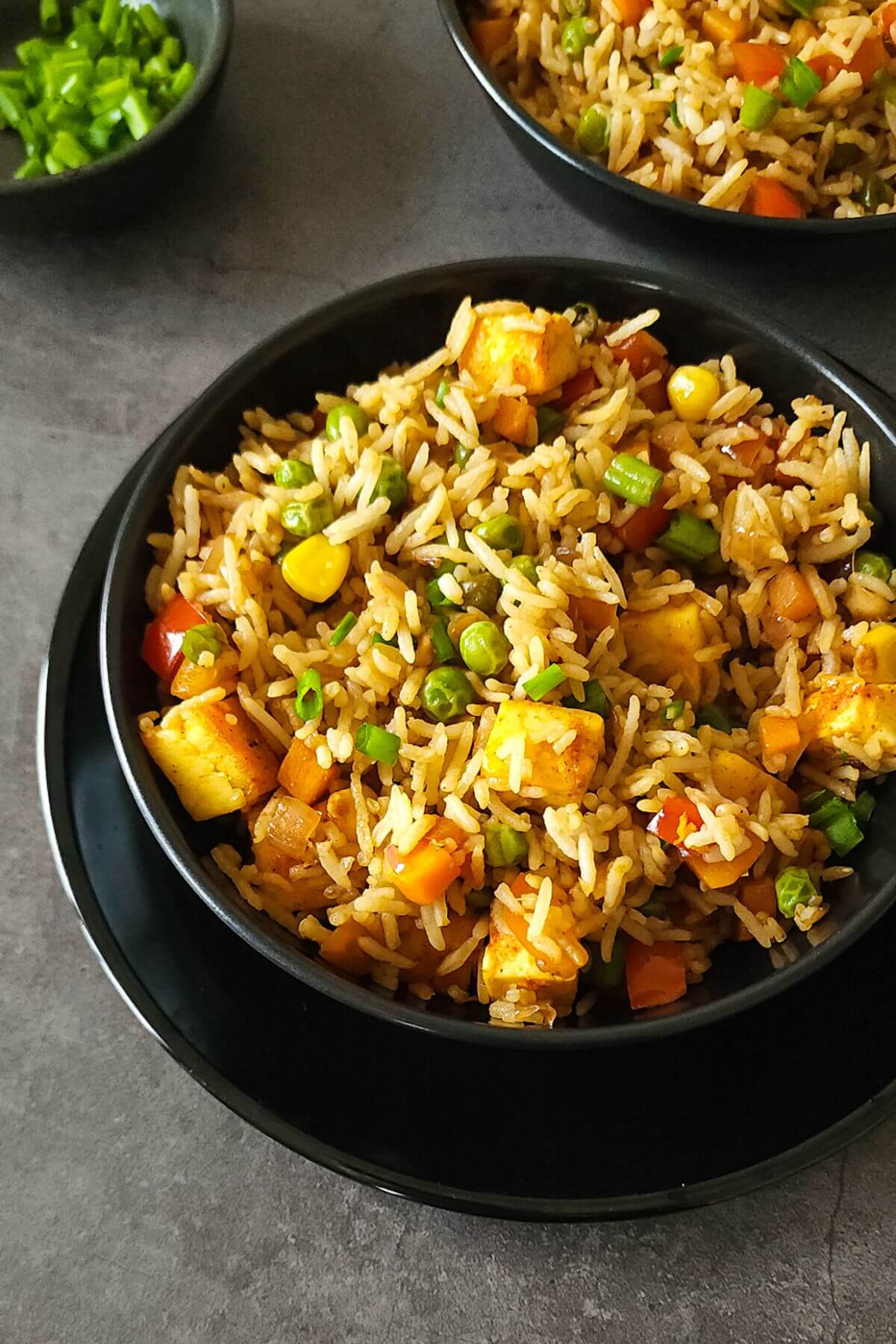 Two bowls of paneer fried rice with chopped spring onion in a bowl.
