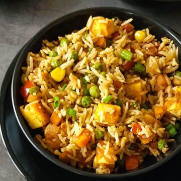 Paneer fried rice with vegetables in a black bowl.