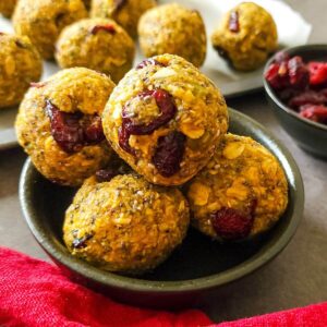 Pumpkin energy balls in a bowl with more balls and dried cranberries in the background.
