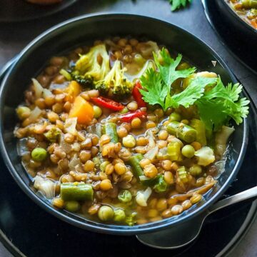 Vegetable lentil soup in a black bowl.