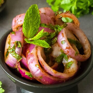 Indian onion salad garnished with mint leaves in a small bowl.