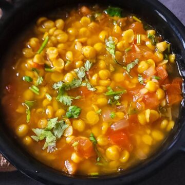 Chana dal garnished with chopped cilantro served in a black bowl.