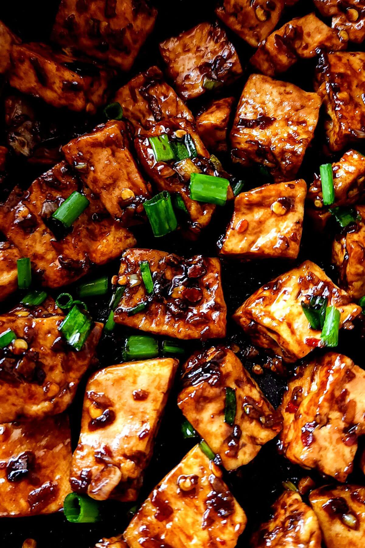 Close up shot of spicy tofu garnished with chopped spring onion greens.