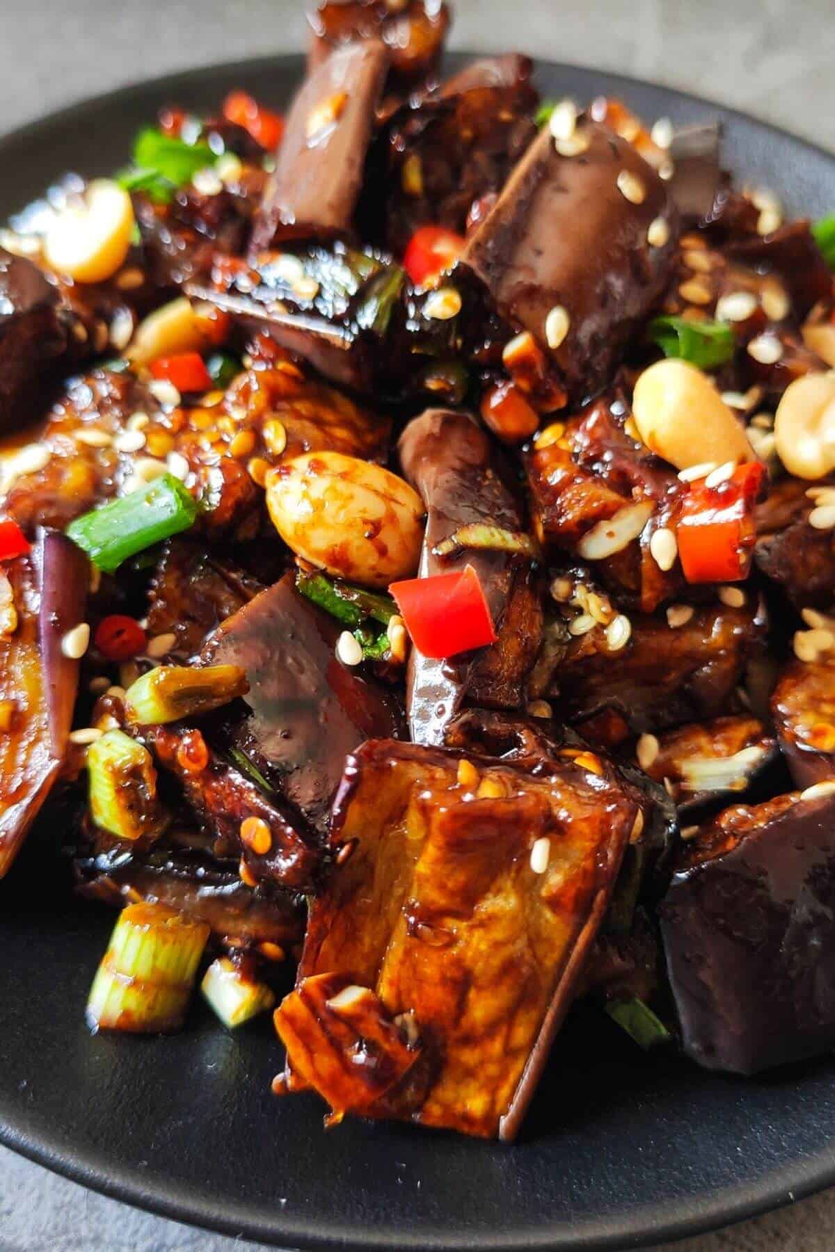 Asian eggplant with garlic sauce served on a black plate.