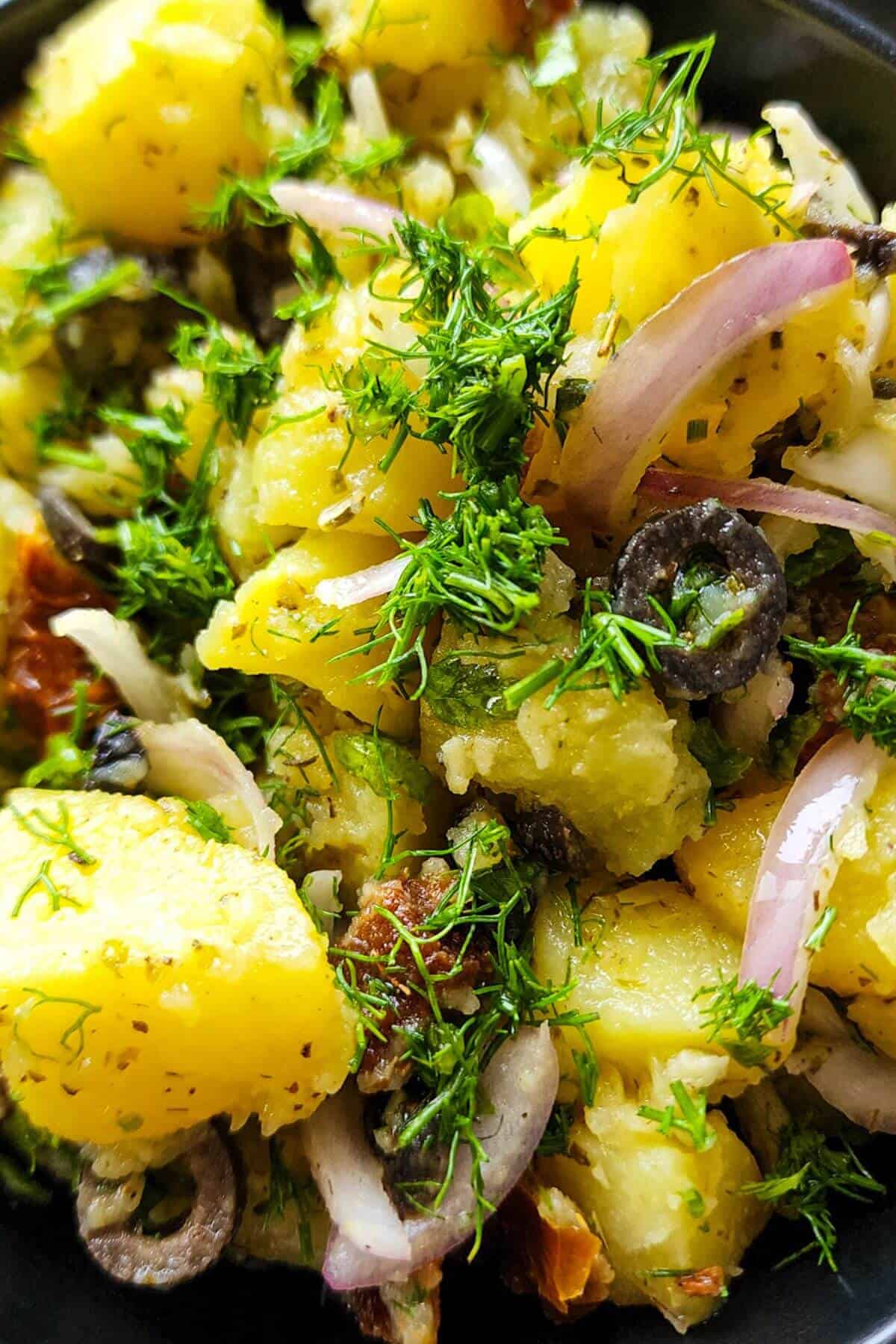 Close up shot of Greek potato salad with onion, sun dried tomatoes, sliced olives, and dill.