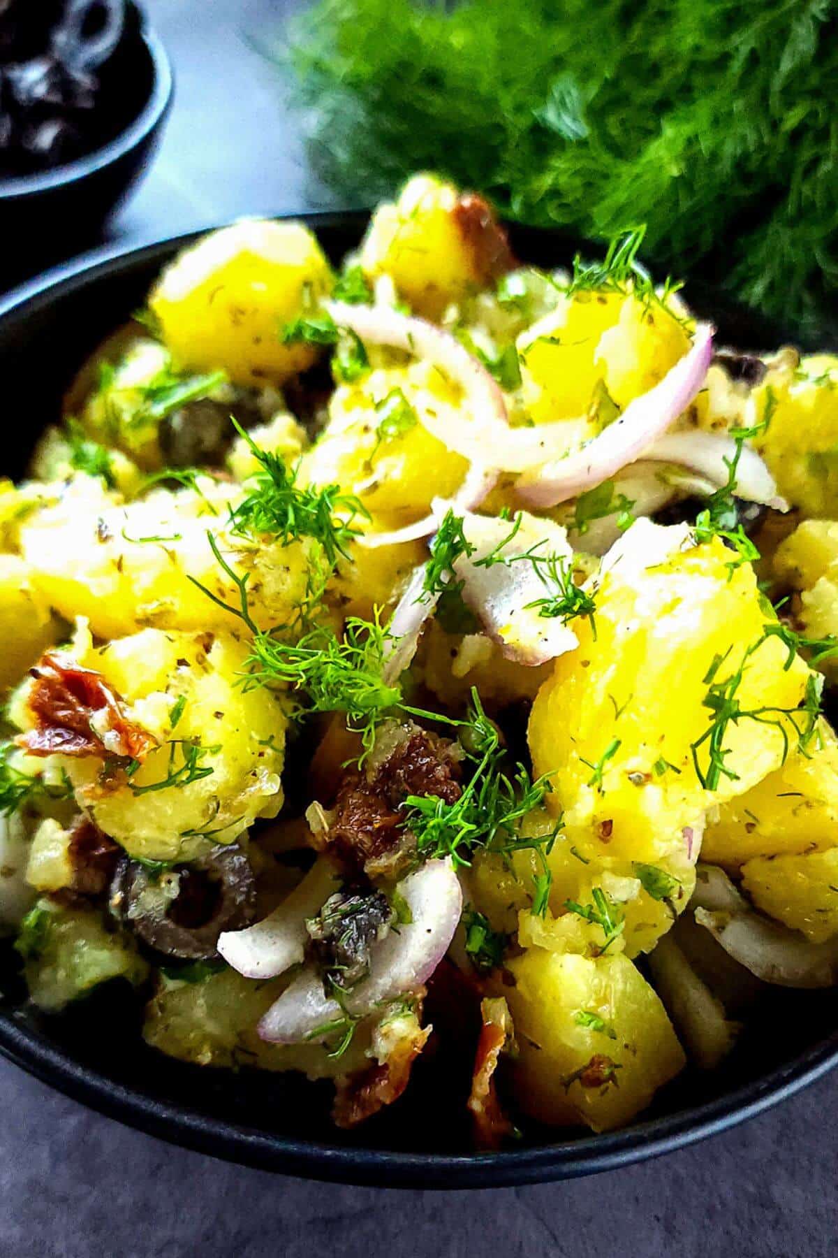 Vegan Greek potato salad garnished with chopped dill in a black bowl.