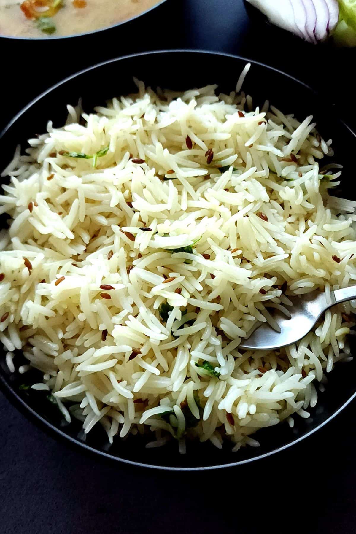 Jeera rice served in a black bowl with a spoon.