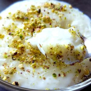 Lebanese rice pudding with chopped pistachios scooped out from a bowl of pudding with a spoon.